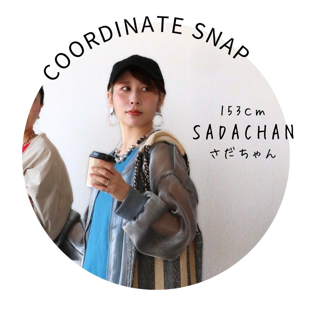 Person posing with drink, wearing a cap and stylish outfit.