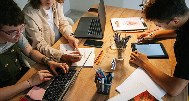 Three people collaborating at a table with laptops and stationery.