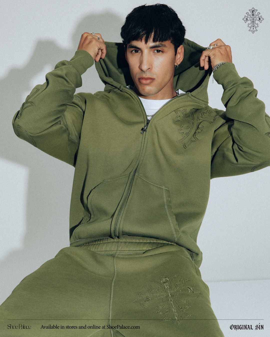 Young man in olive green hoodie, posing with hood up.