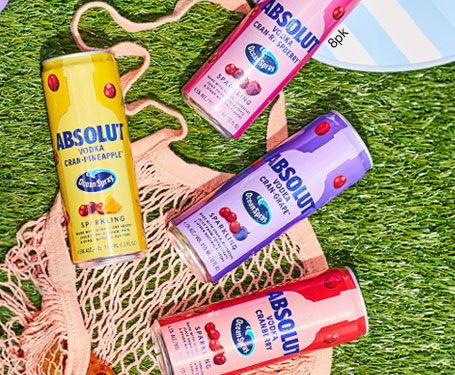 Four cans of Absolut drinks on grass with a bag.
