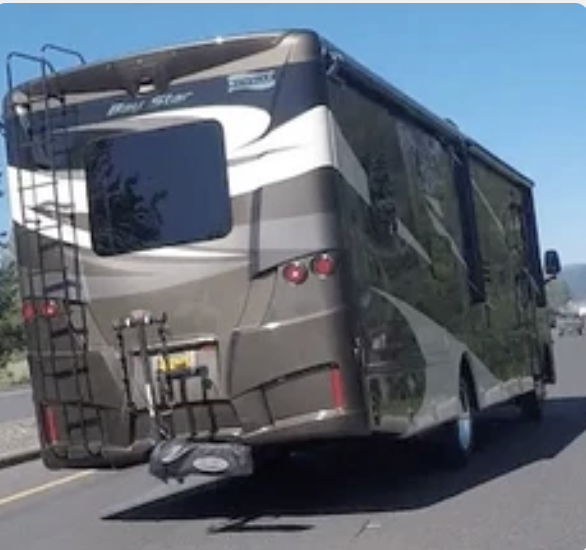 A large RV driving on a road with clear blue skies.