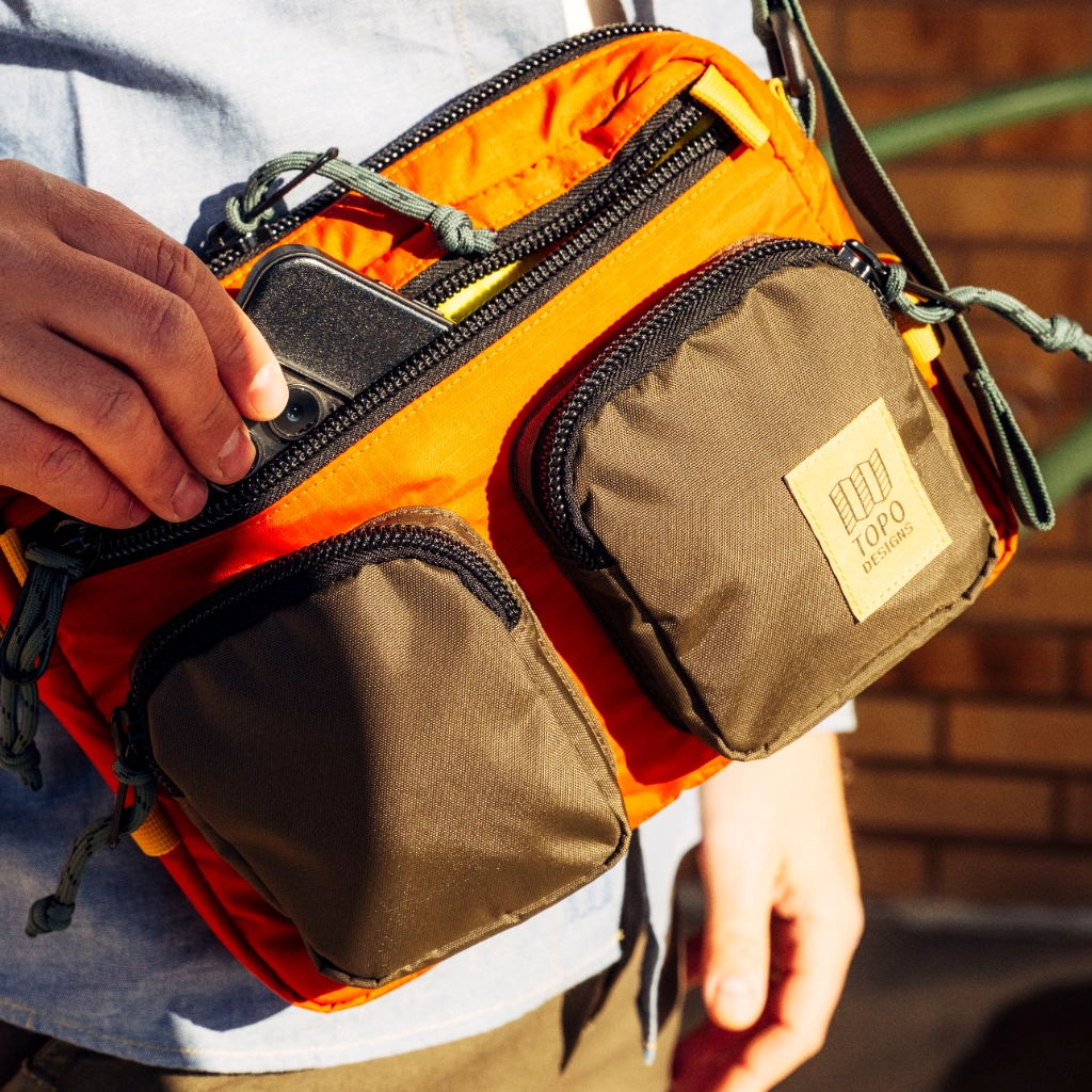 Person holding an orange and brown crossbody bag with multiple pockets.
