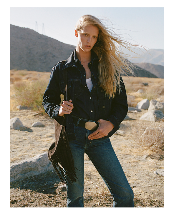 A woman in casual attire stands in a desert landscape.