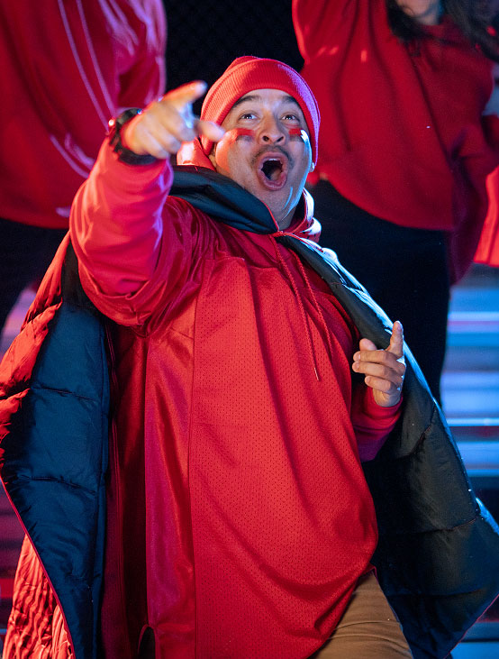 A person in a red outfit gestures enthusiastically while performing.
