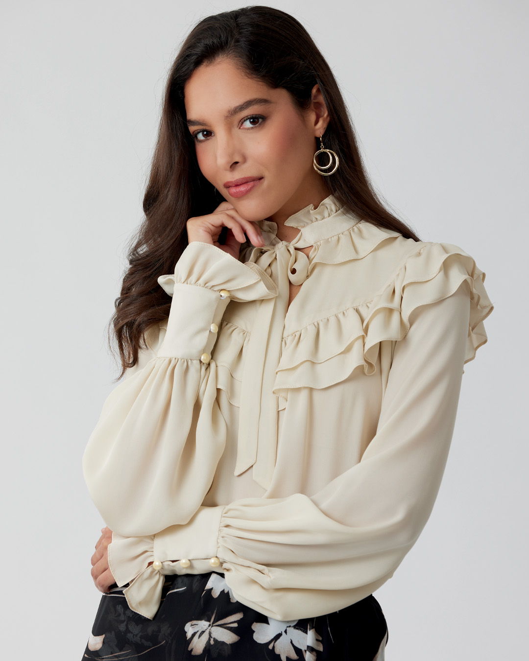 A woman in a ruffled cream blouse poses confidently.