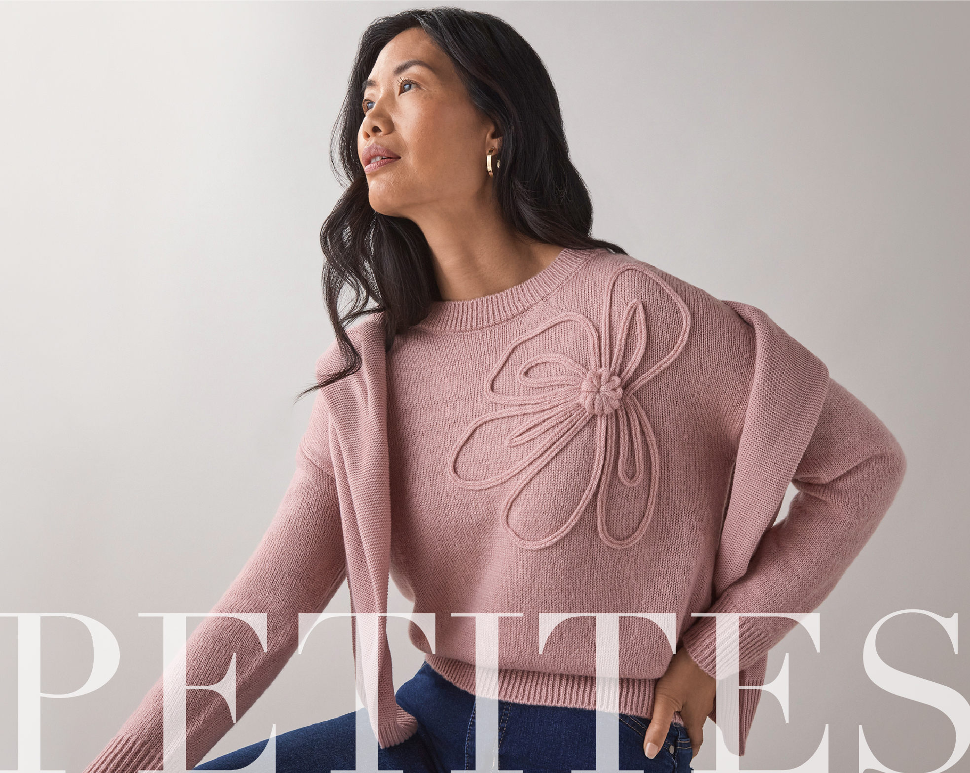 A woman wearing a pink sweater with a floral design, looking to the side.