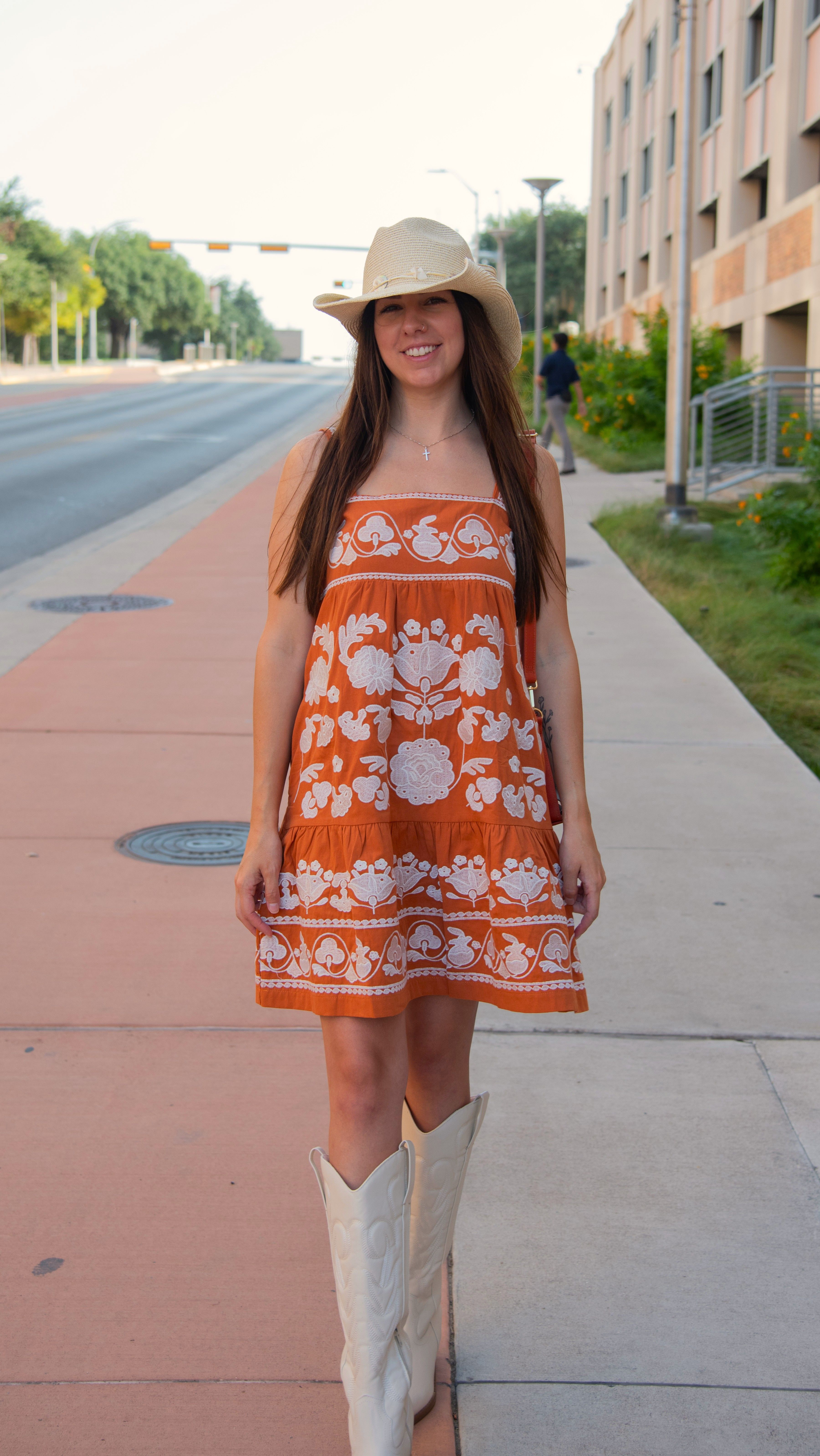 Woman in a floral orange dress and cowboy hat on a city sidewalk.