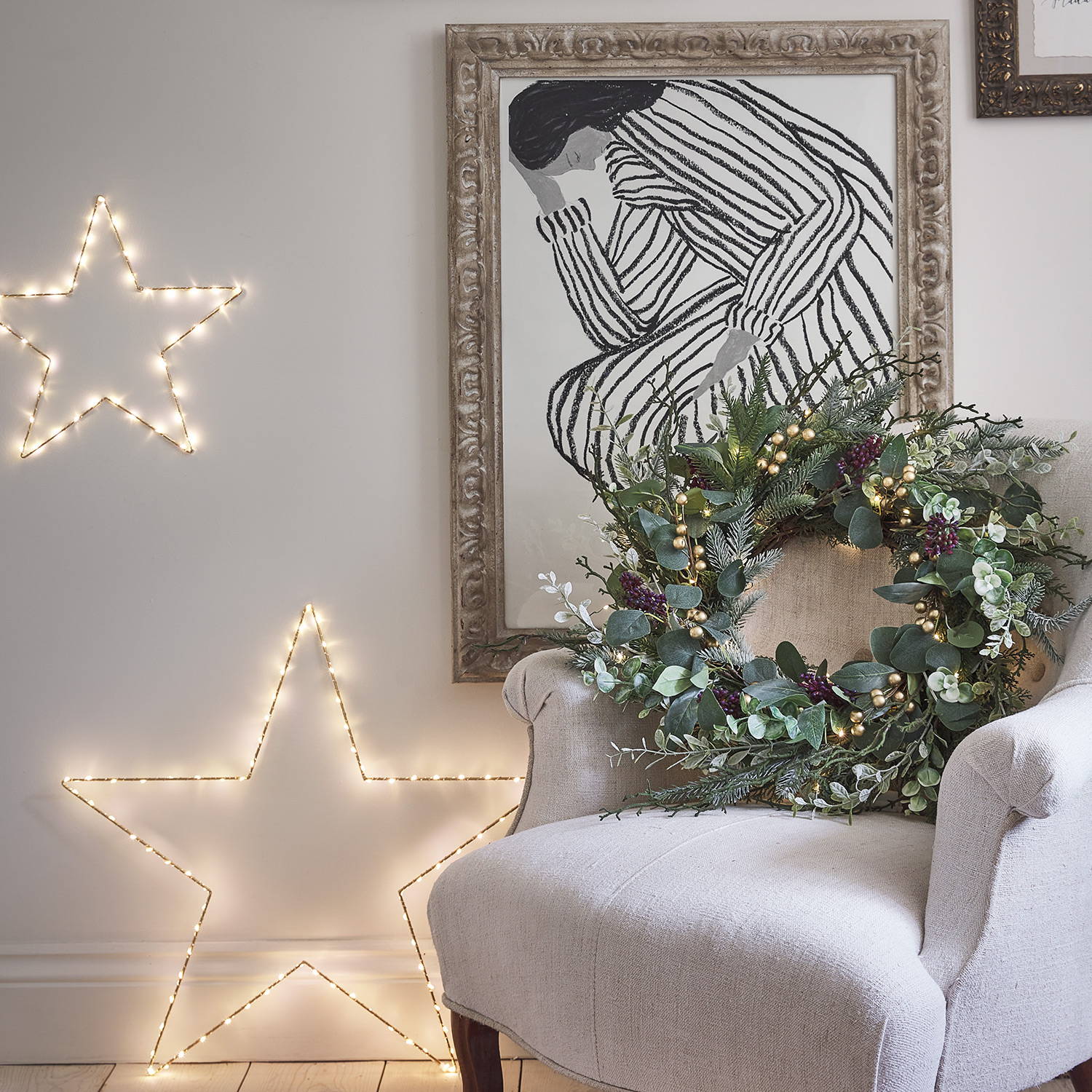 Golden star lights resting against a living room wall, and an armchair decorated with a wreath 