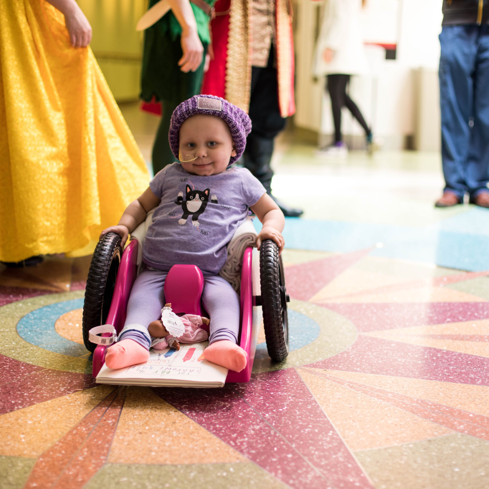 Small girl in a wheelchair wearing a Love Your Melon Beanie and a breathing tube