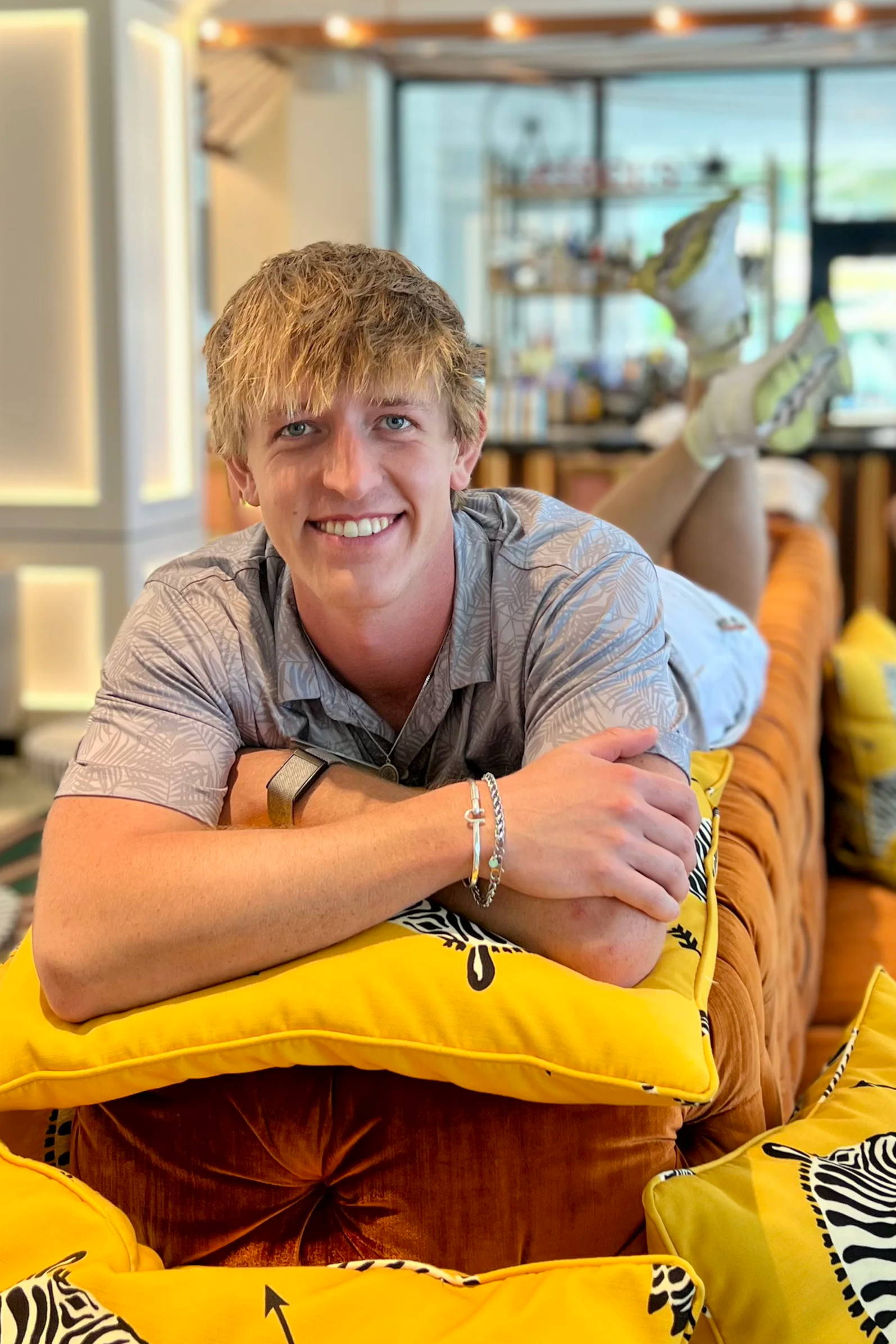 Smiling person lounging on a couch with zebra-patterned pillows.