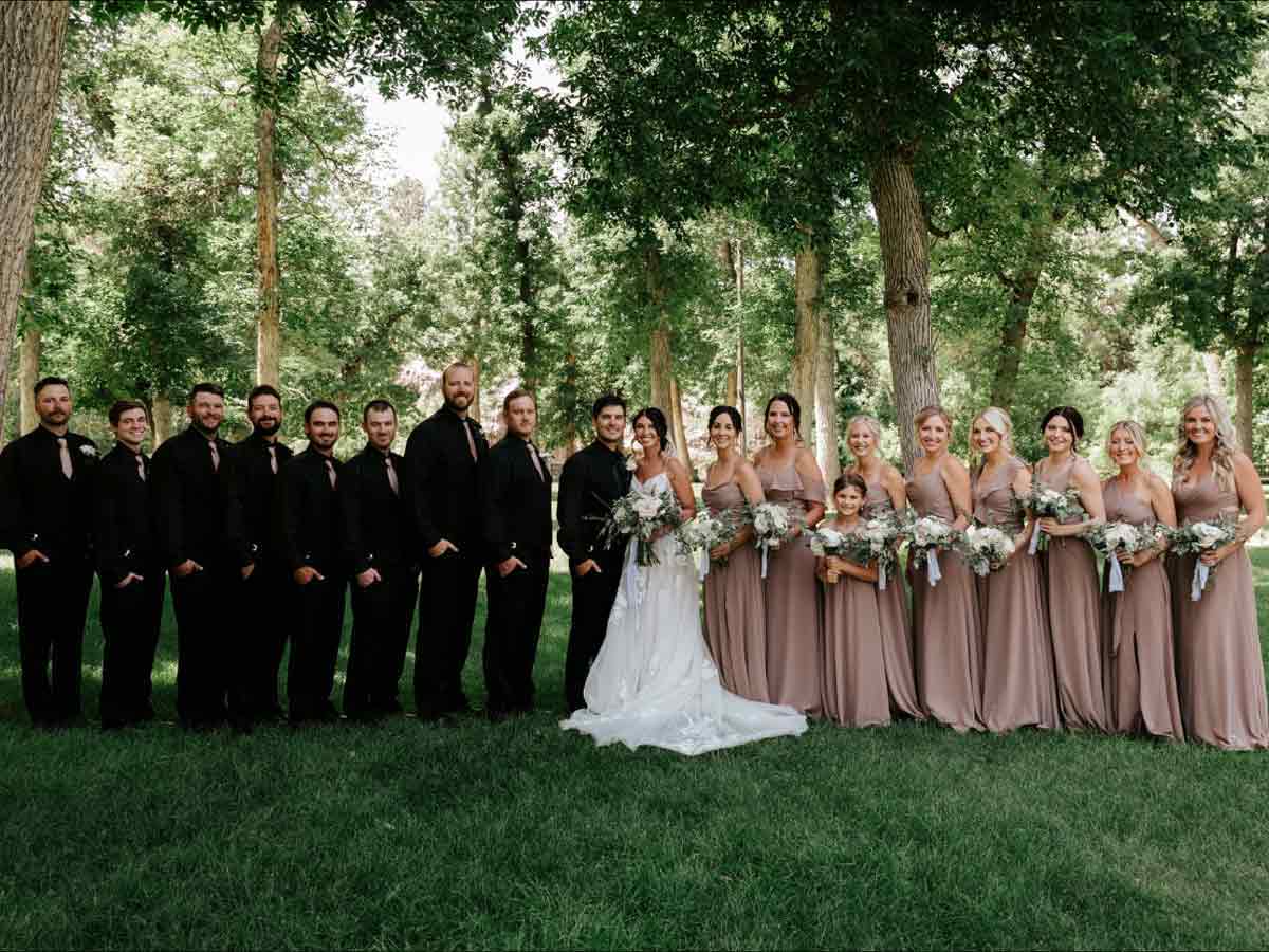A large wedding party posing outside in neutral taupe and black colors