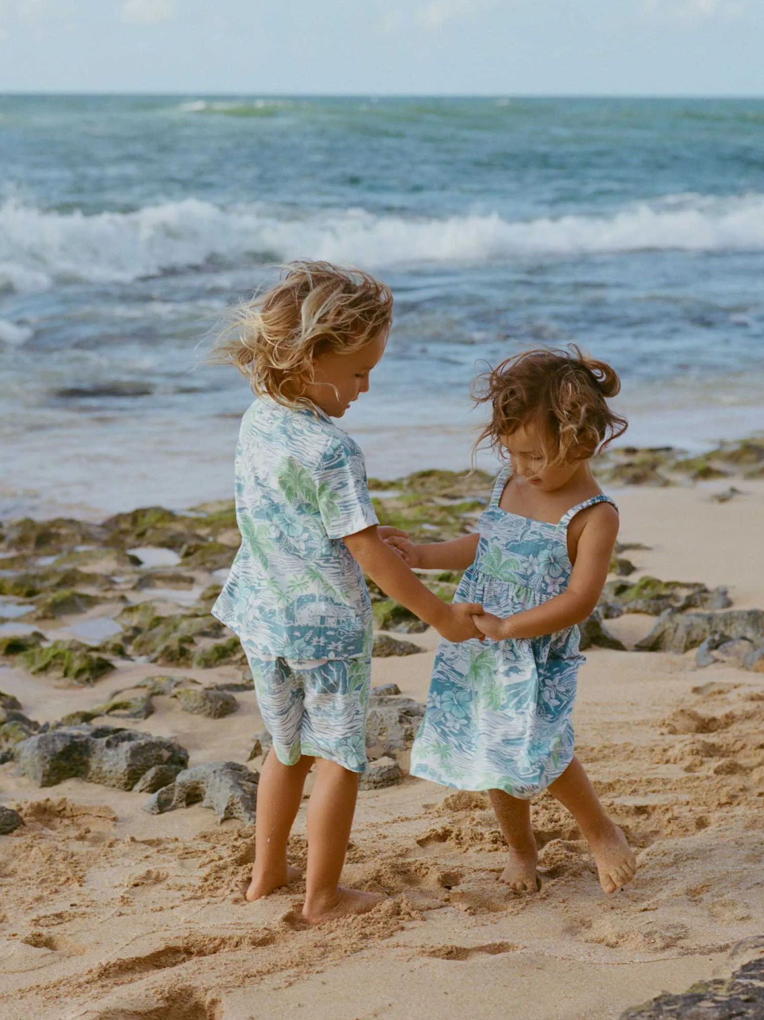 Children playing outside in matching tropical outfits, holding toys.