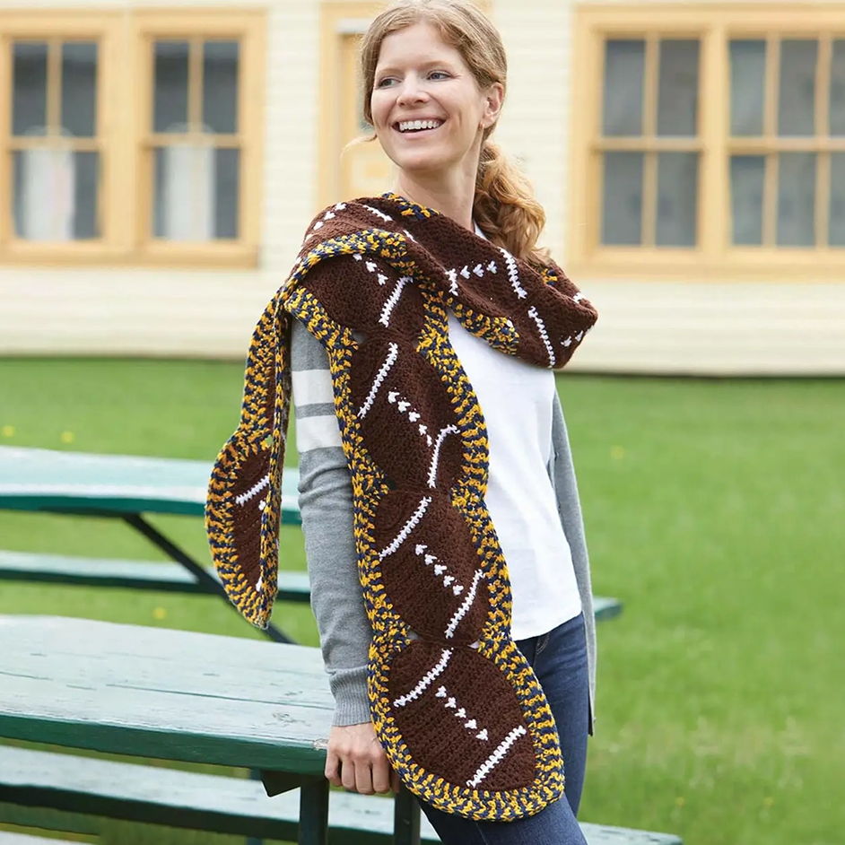 Smiling woman wearing a brown and yellow football shawl outdoors.