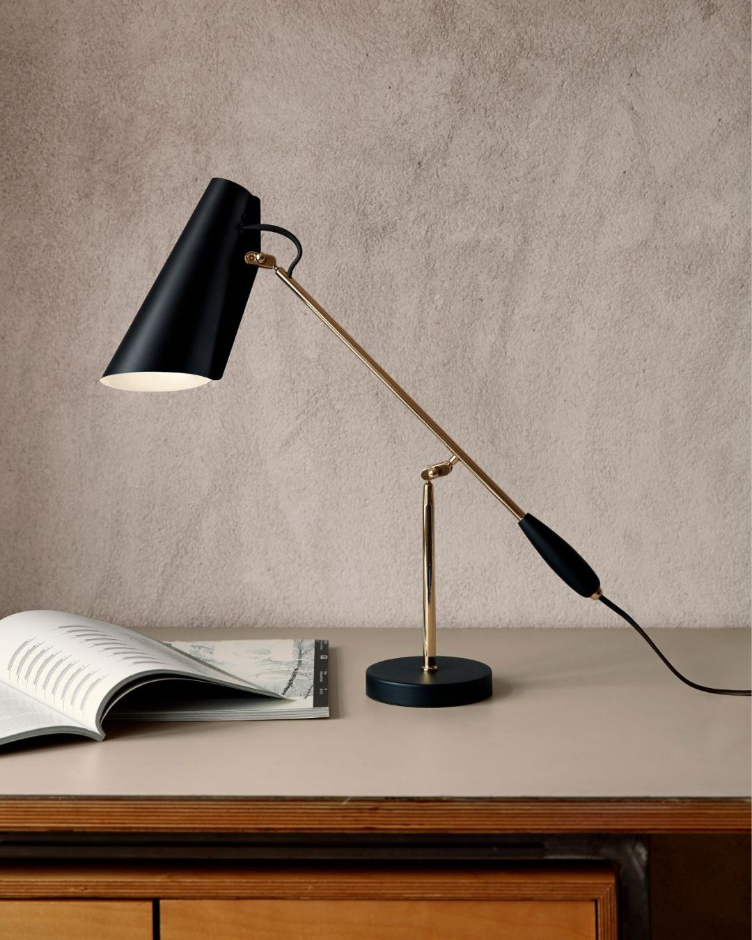 Mid-Century Adjustable Table Lamp on a wooden surface with an open book in the background.
