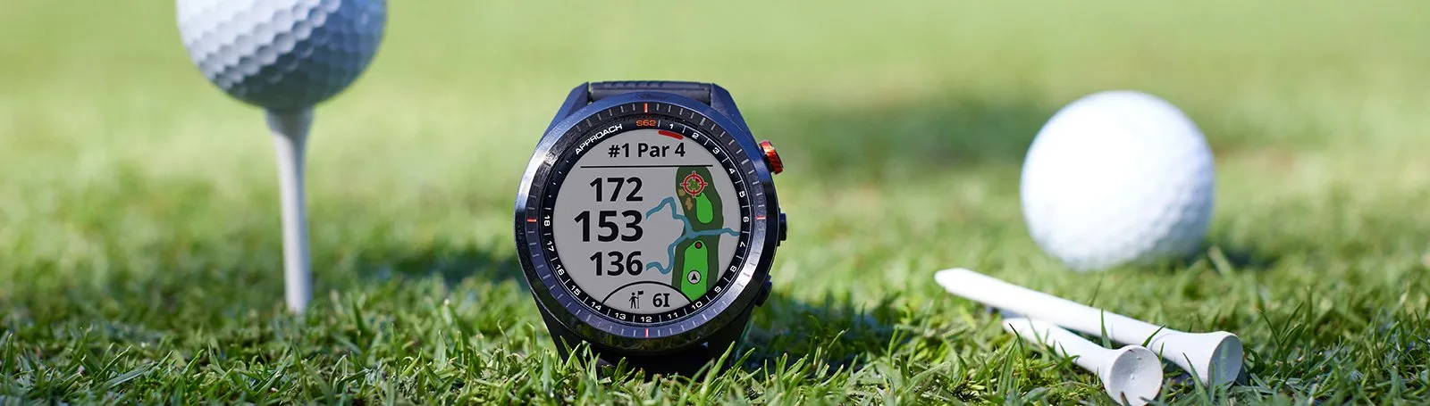A Garmin Approach S62 on the grass of a golf course next to golf tees and golf balls
