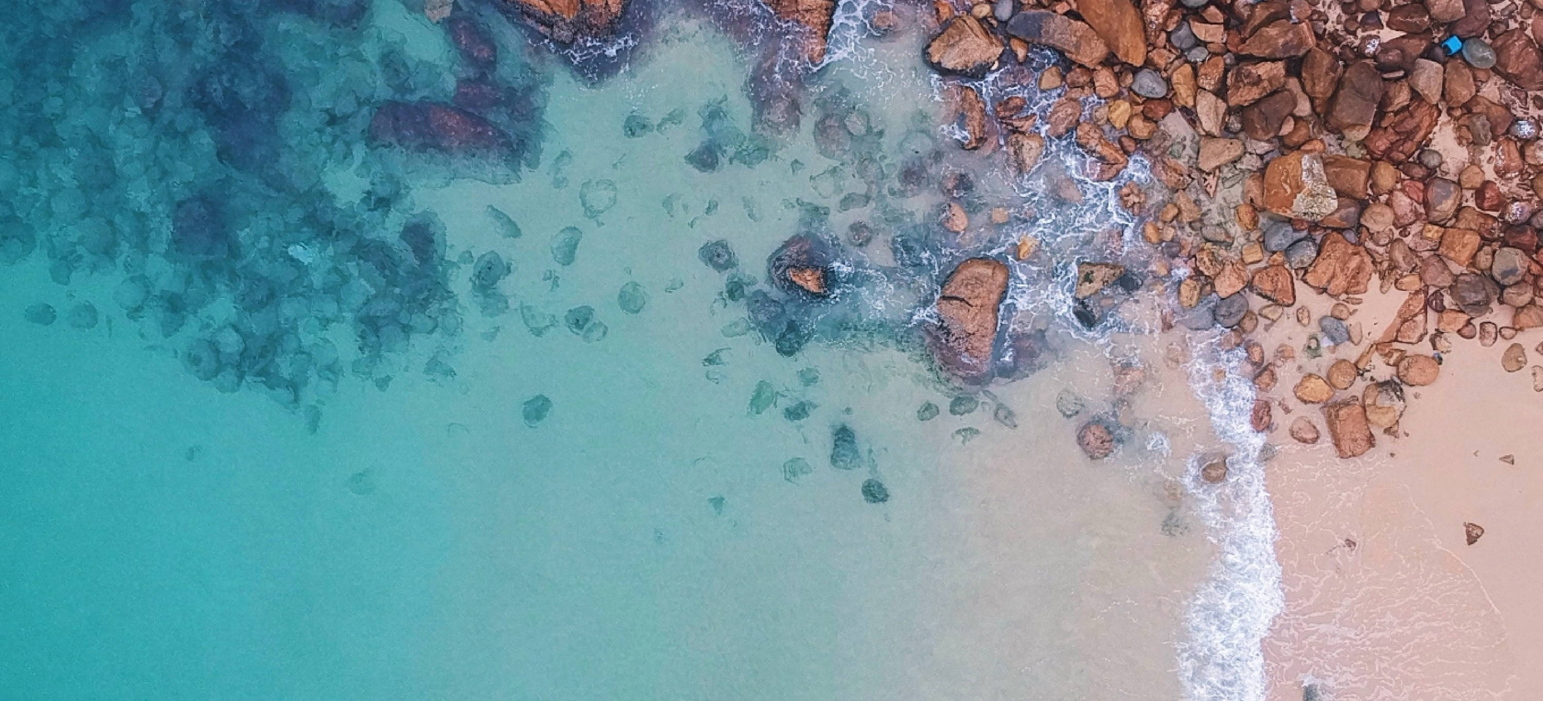 aerial shot of blue water at beach with rocks and sand CAMILLA Reducing our footprint