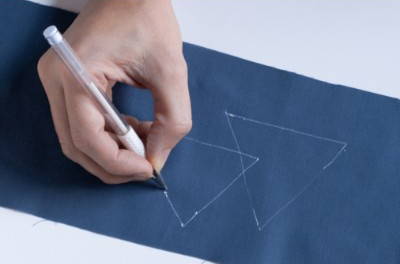 image of a white heat erasable fabric marking pen being tested on a piece of blue fabric