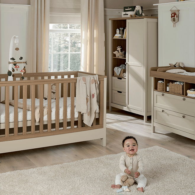 Baby sitting on rug in a nursery with crib and furniture.