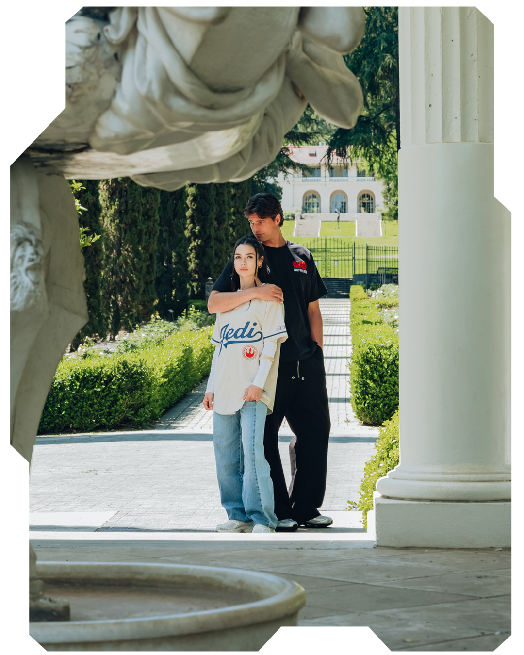 A couple poses together near a statue in a garden setting.