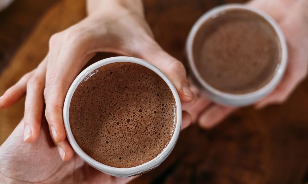 Two hands holding cups of hot chocolate or coffee.