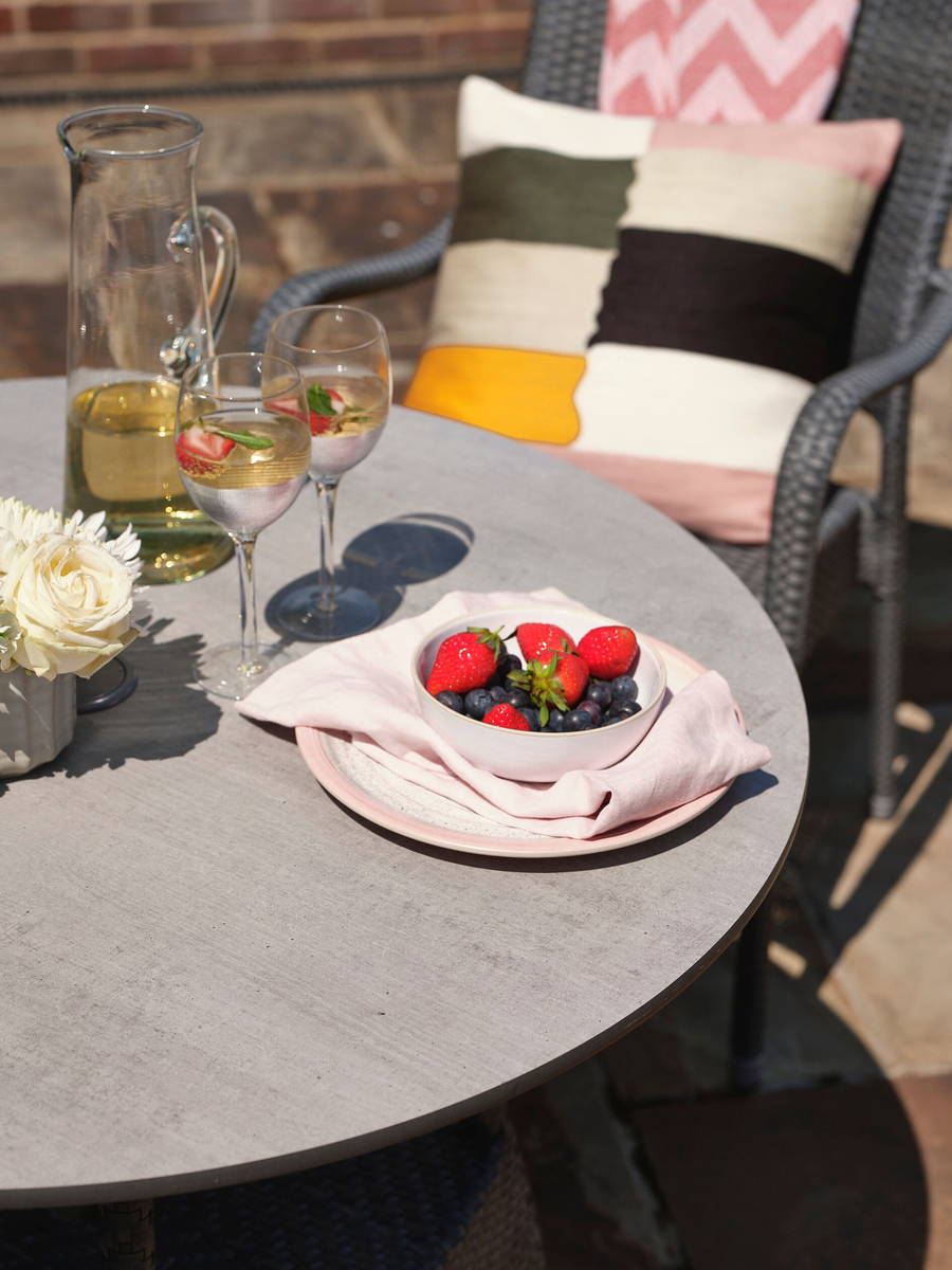 Grey garden dining table with concrete effect with a bowl of fruit and wine.