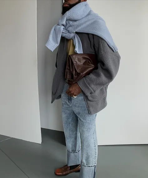 Person wearing a gray jacket, blue scarf, and holding a brown clutch.