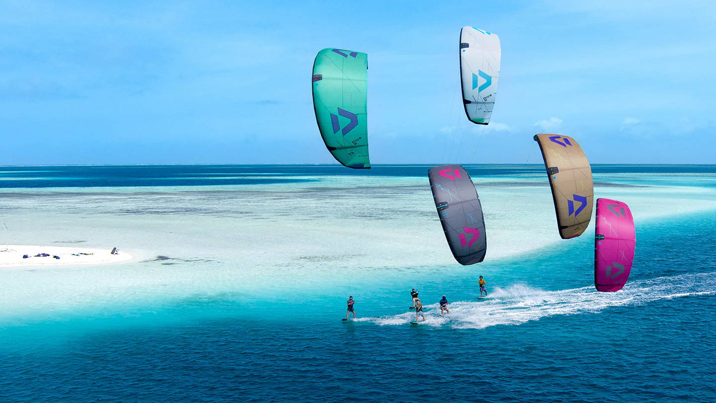 Des kitesurfeurs sur des eaux d'un bleu éclatant près d'une plage de sable.