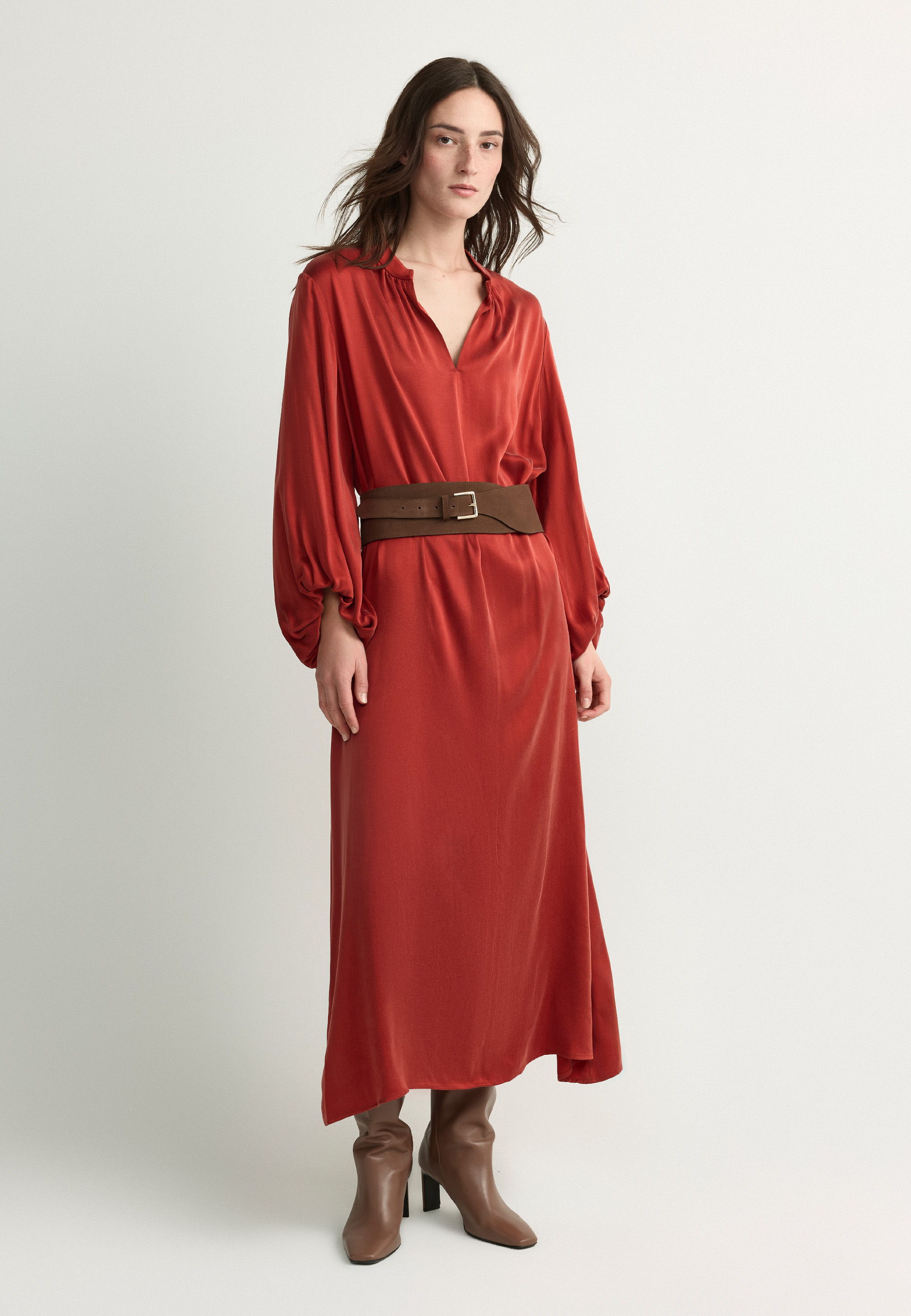 Woman in a long red dress with a belt and brown boots.