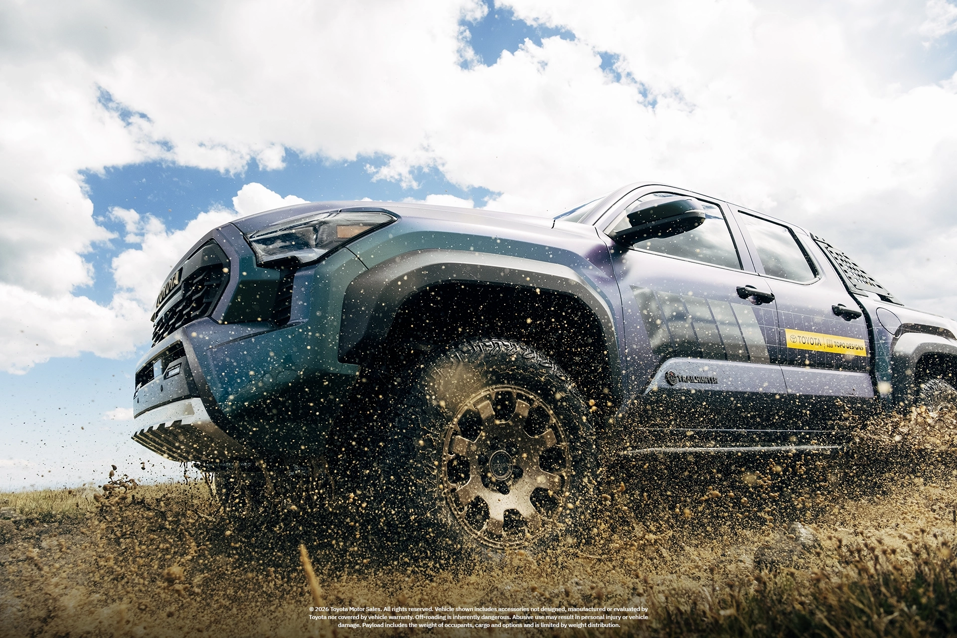 Off-road truck splashing through mud under a cloudy sky.