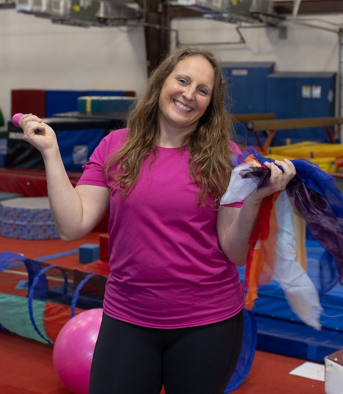 Woman in a pink shirt holding colorful ribbons in a gym environment.