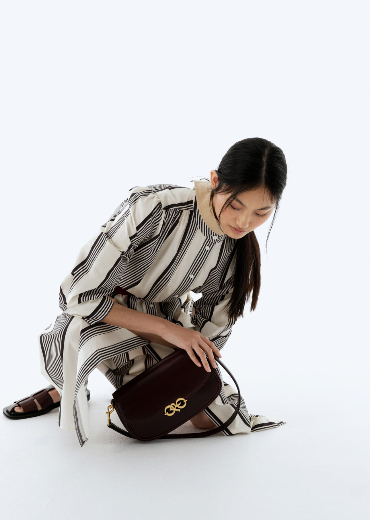 A woman in a striped dress crouches to retrieve a handbag.
