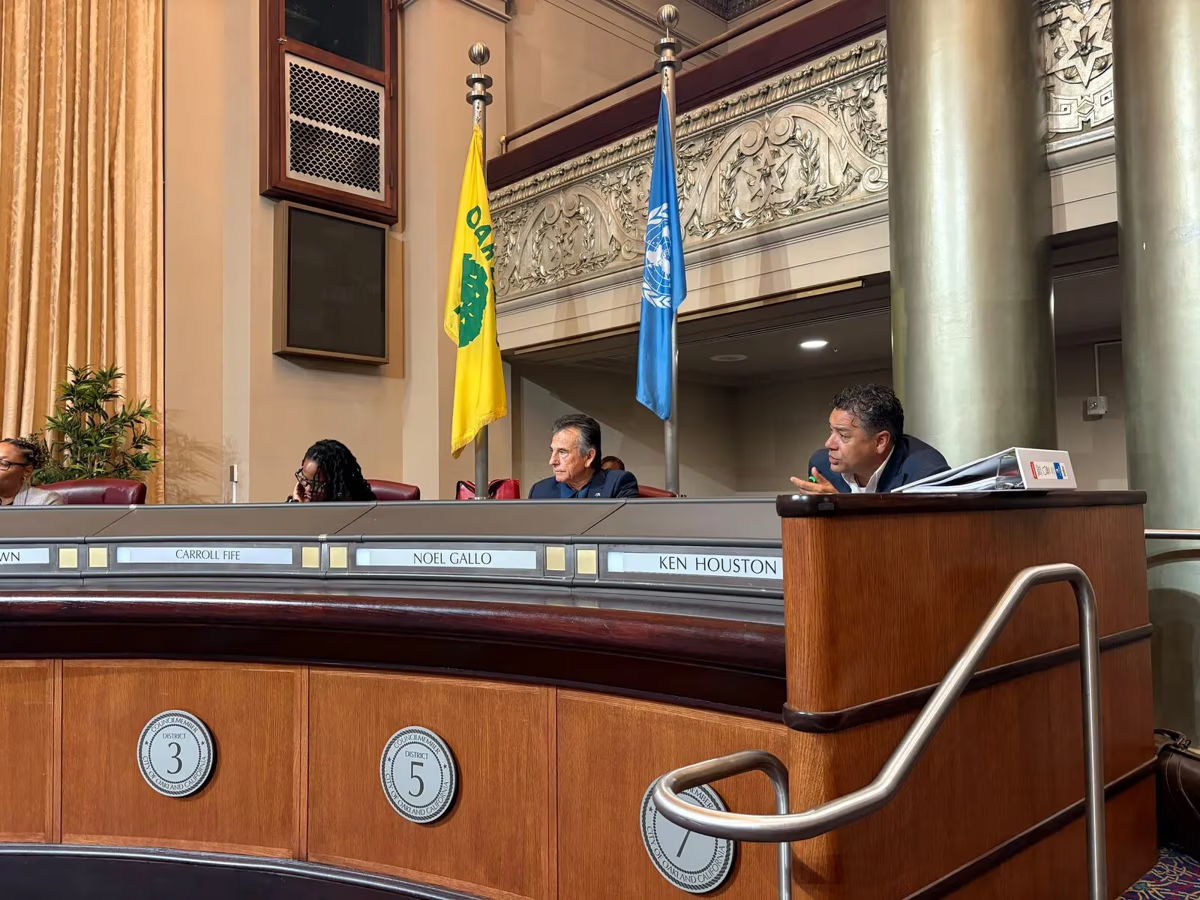 A meeting room with officials seated at a curved table, flags in background.