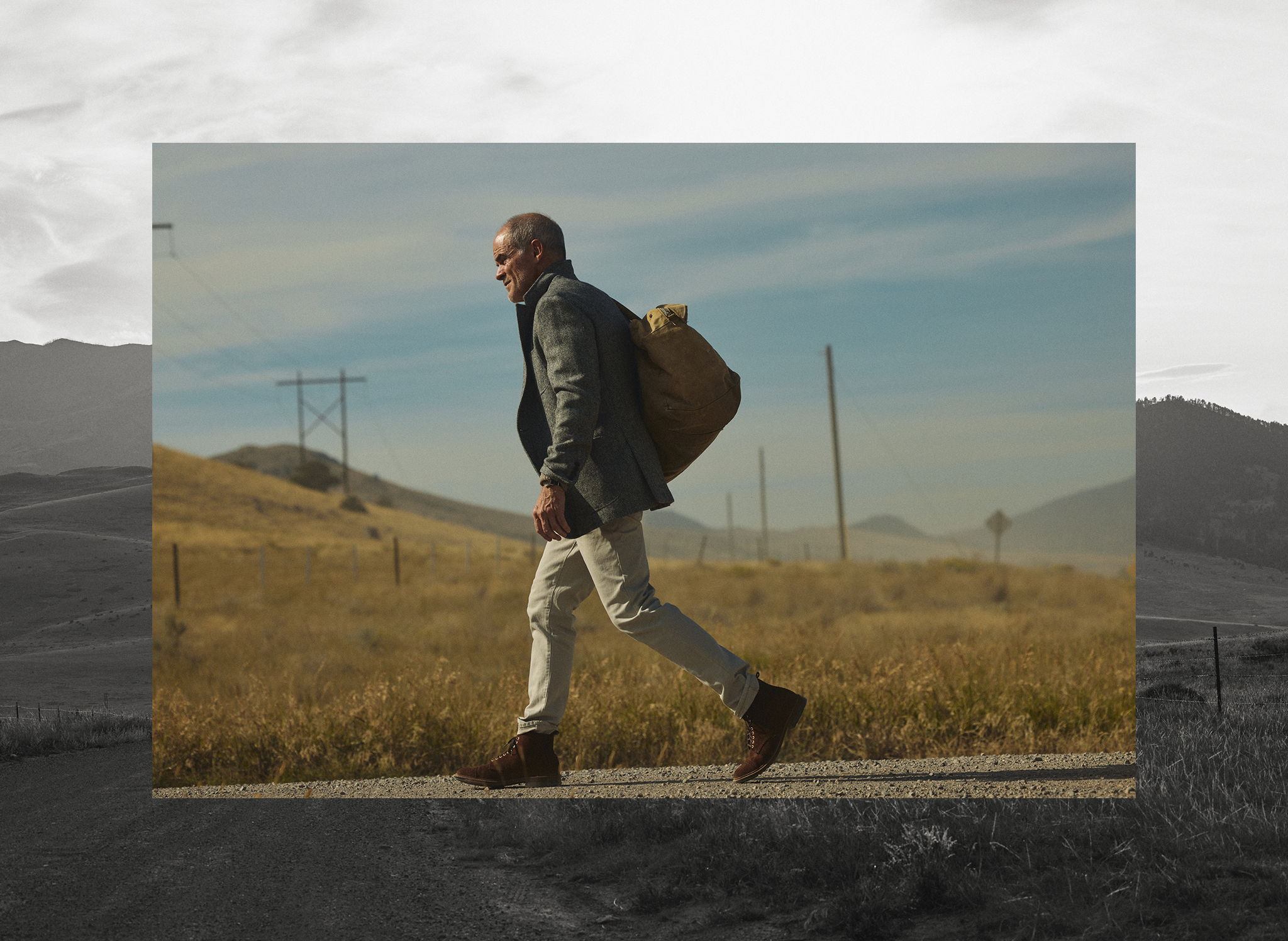 Michael Kelly walking down a gravel road wearing the Rivay Stanton Wool Herringbone Tweed Sportcoat over the Sonny Waffle Sweater in Khaki Marl with the WWade Garment Dyed Five Pocket Pant in Stone Grey holding a vintage air force pilots kit bag in Emigrant, Montana