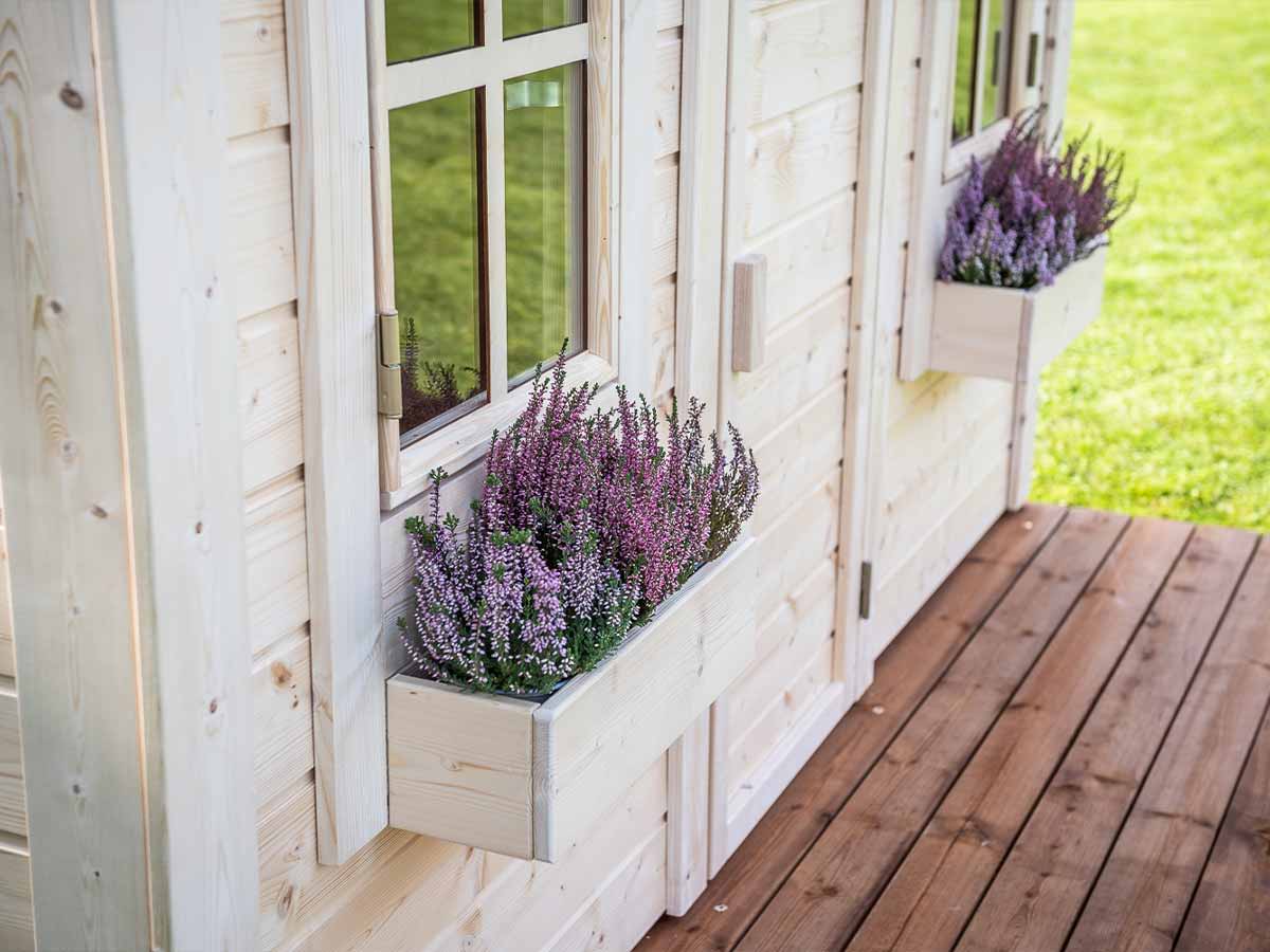 Close-up of the flower boxes with flowers and wooden terrace of Outdoor Playhouse Natural Wonder in a backyard by WholeWoodPlayhouses