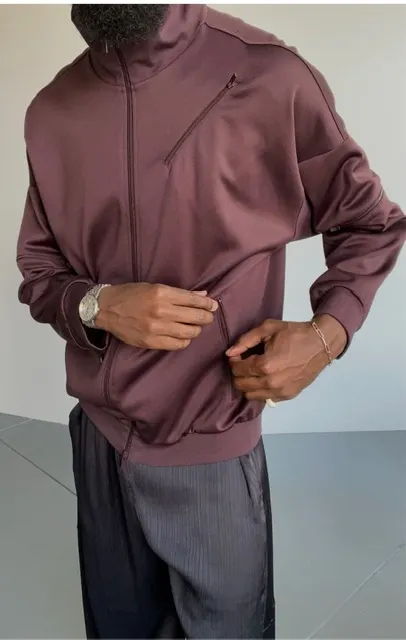 Person adjusting a maroon zip-up jacket, wearing gray pants.