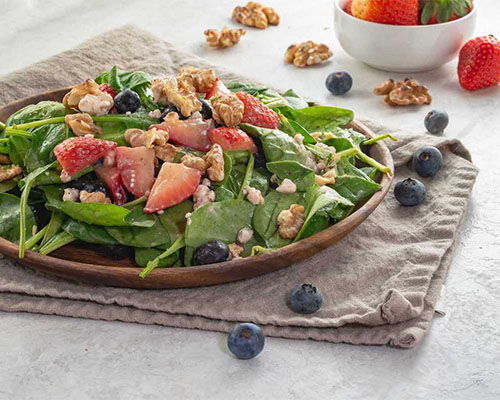 A fresh salad with spinach, apples, walnuts, and blueberries on a wooden plate.