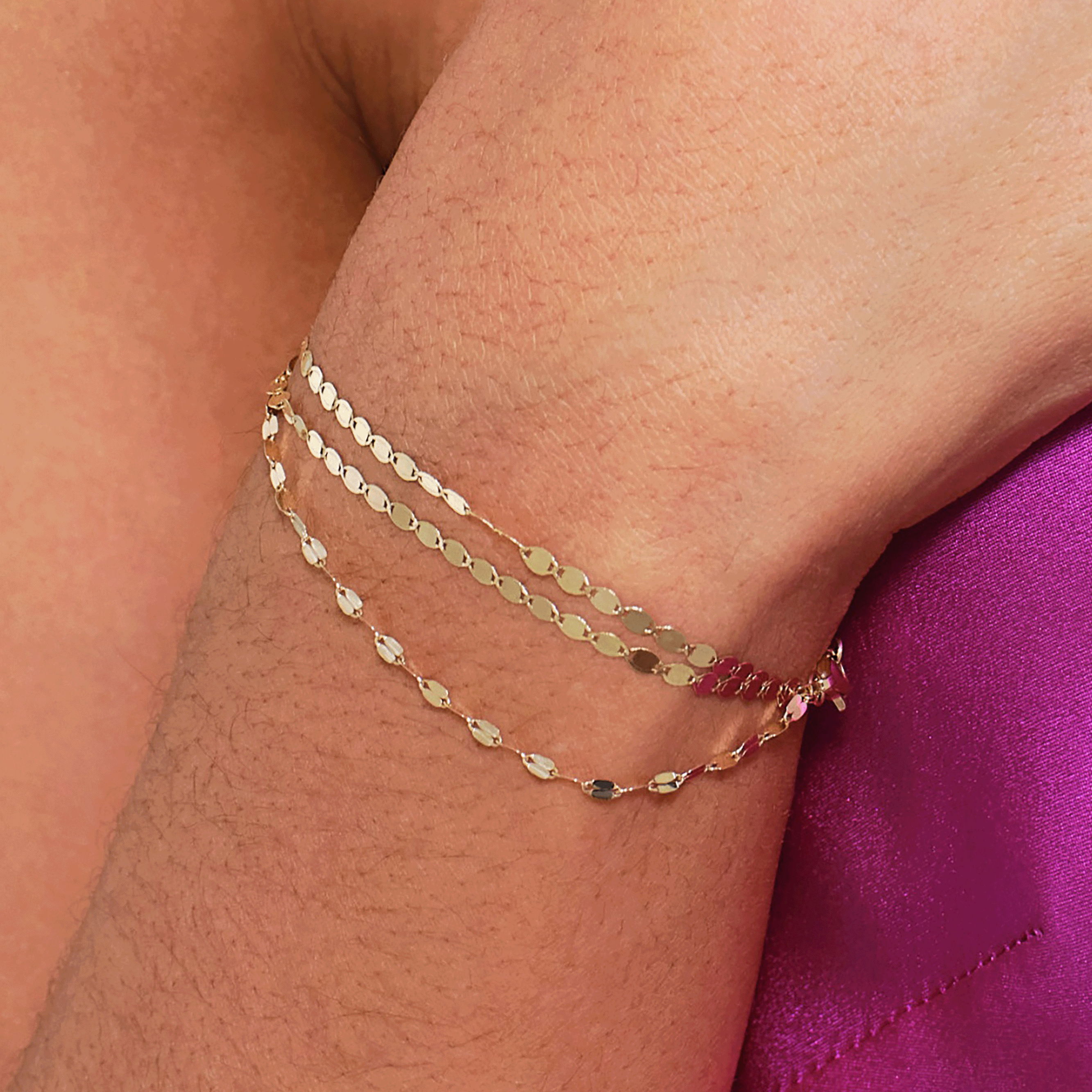 Close-up of a wrist wearing layered yellow gold chain bracelets with delicate oval links for an everyday stacked look.