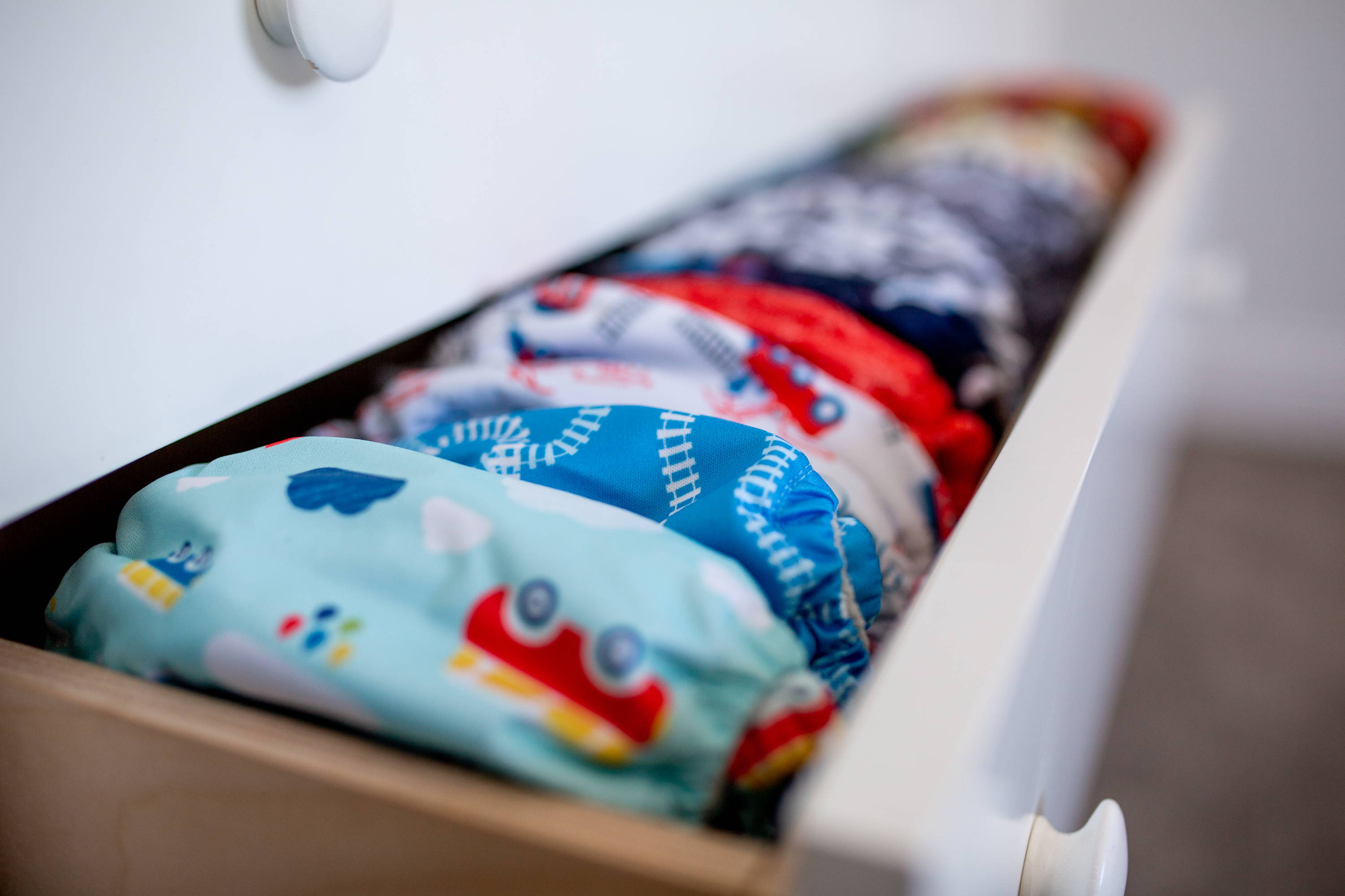 Drawer full of planes/trains themed cloth diapers looking colorful behind our black and white text saying 