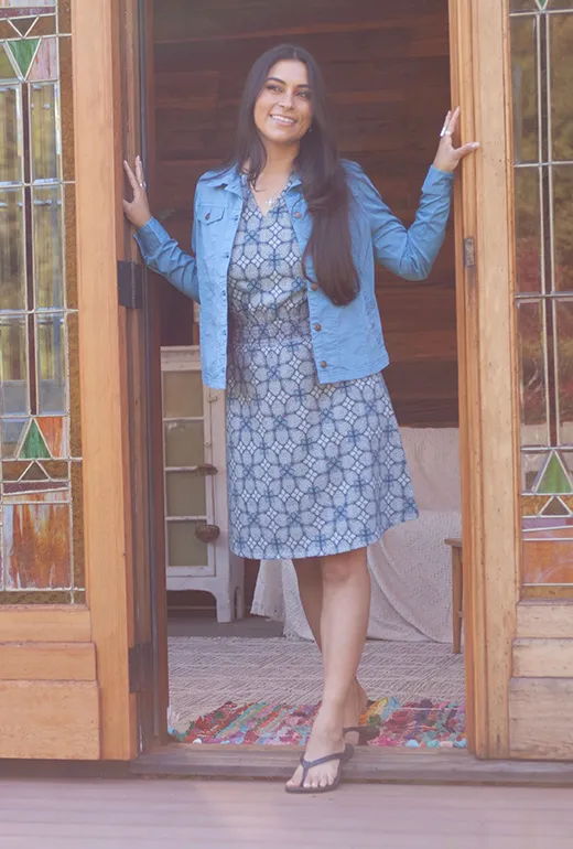Woman in a denim jacket standing at an open door, smiling.