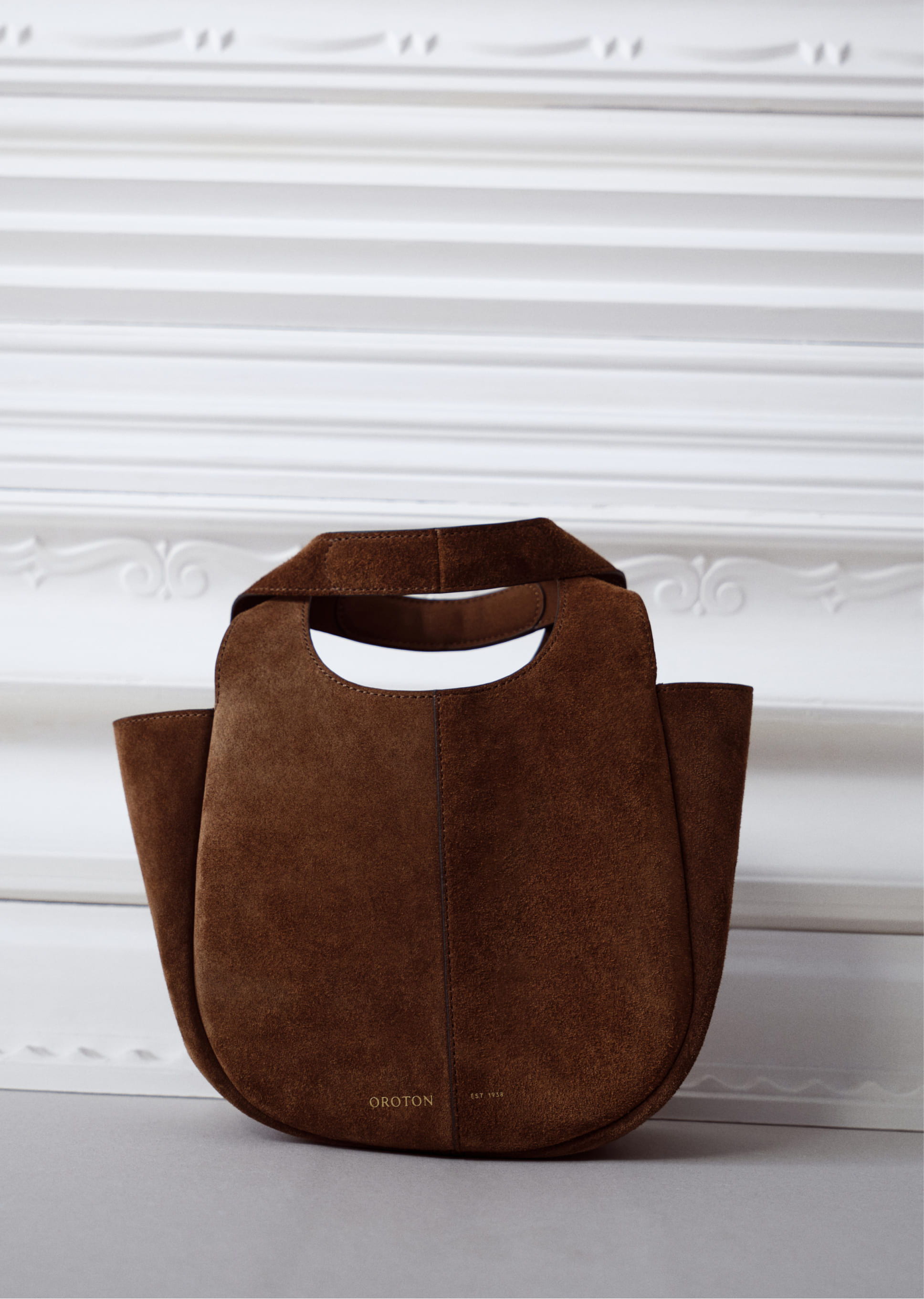Brown suede handbag with unique handle design against a white background.