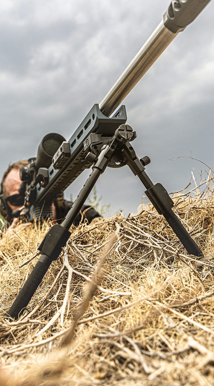 A sniper rifle on a bipod, with a shooter in the background.