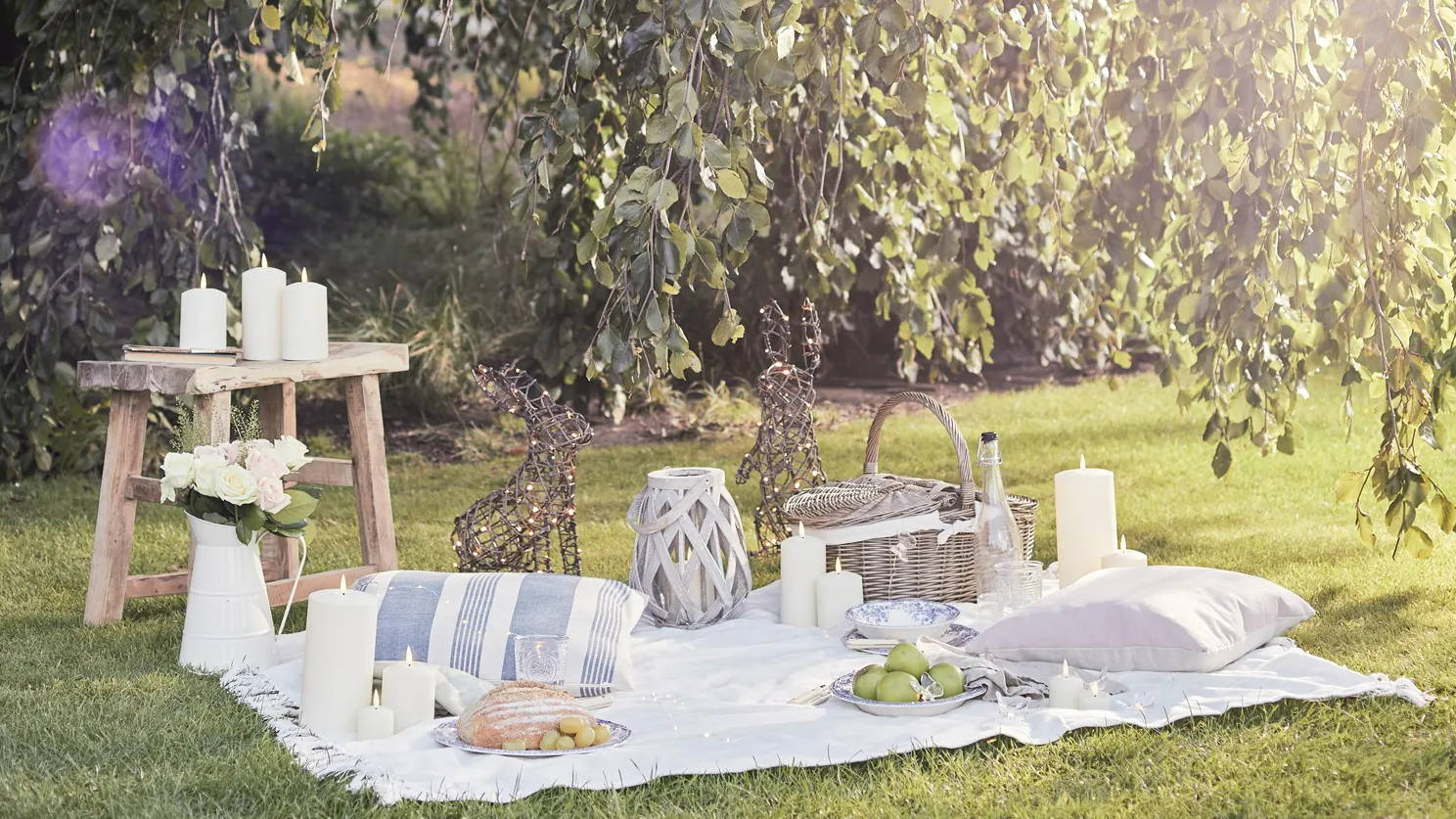 A summer picnic setting with LED candles, lanterns and rattan bunny  figures.
