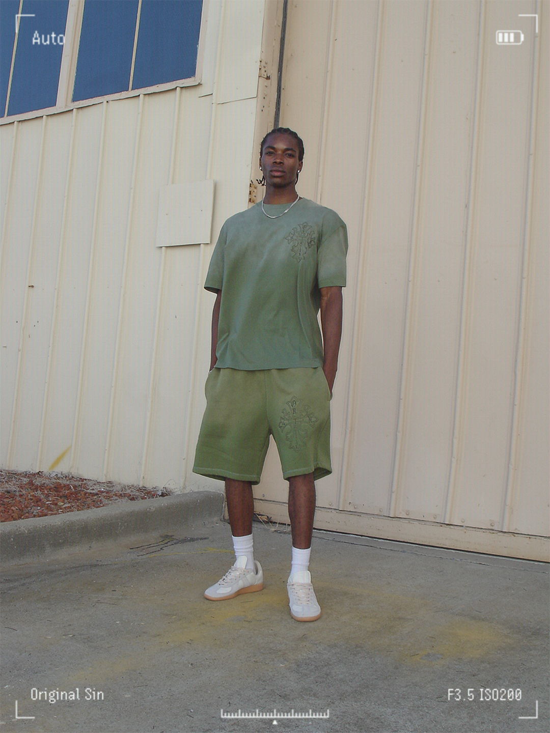 A person standing in green attire against a building backdrop.