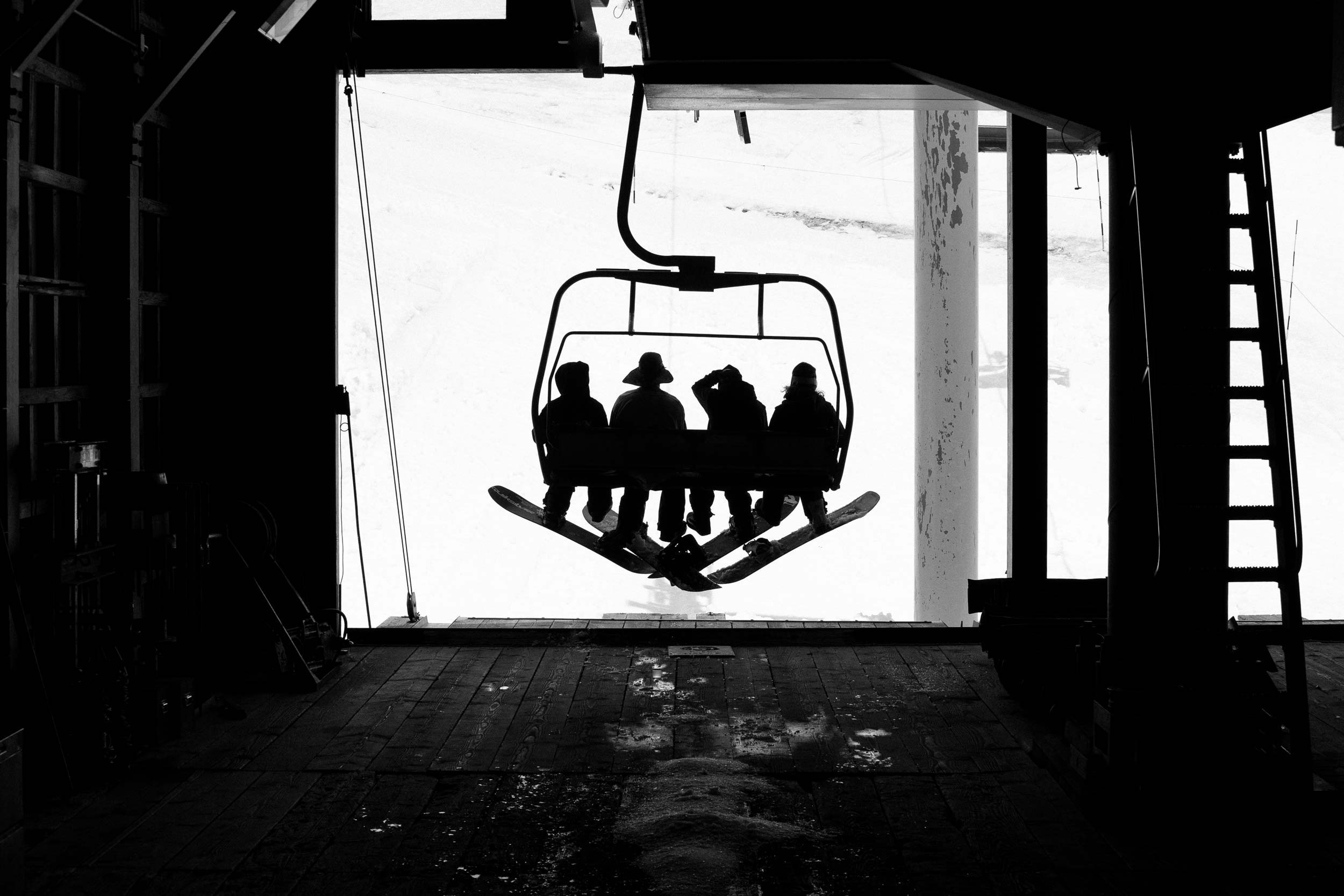 Silhouettes of four people on a ski lift against a bright background.