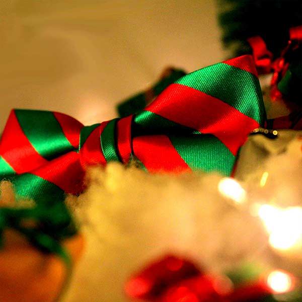 A child-size red and green striped bow tie photographed in warm lighting with holiday props