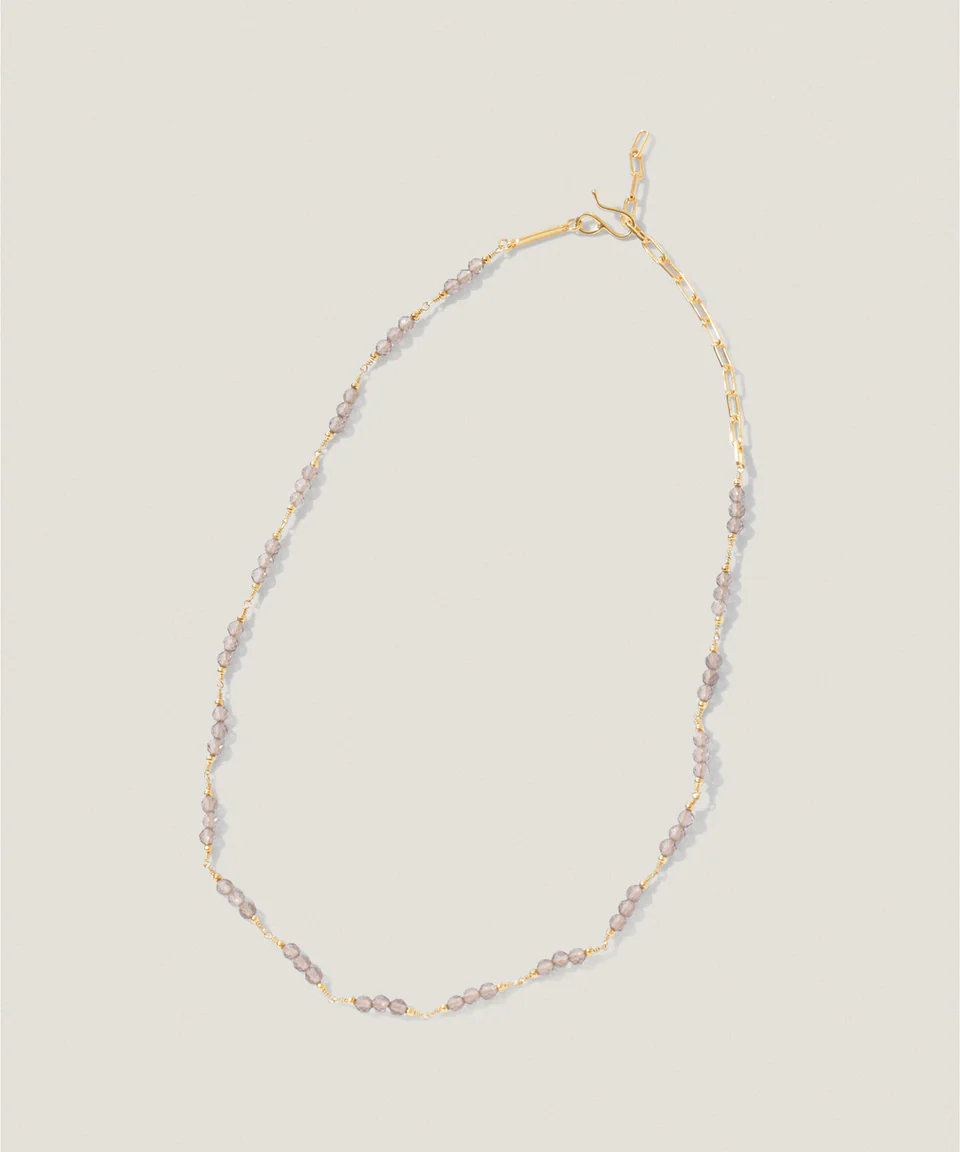 Gold necklace with small gemstones, elegantly twisted design on a light background.