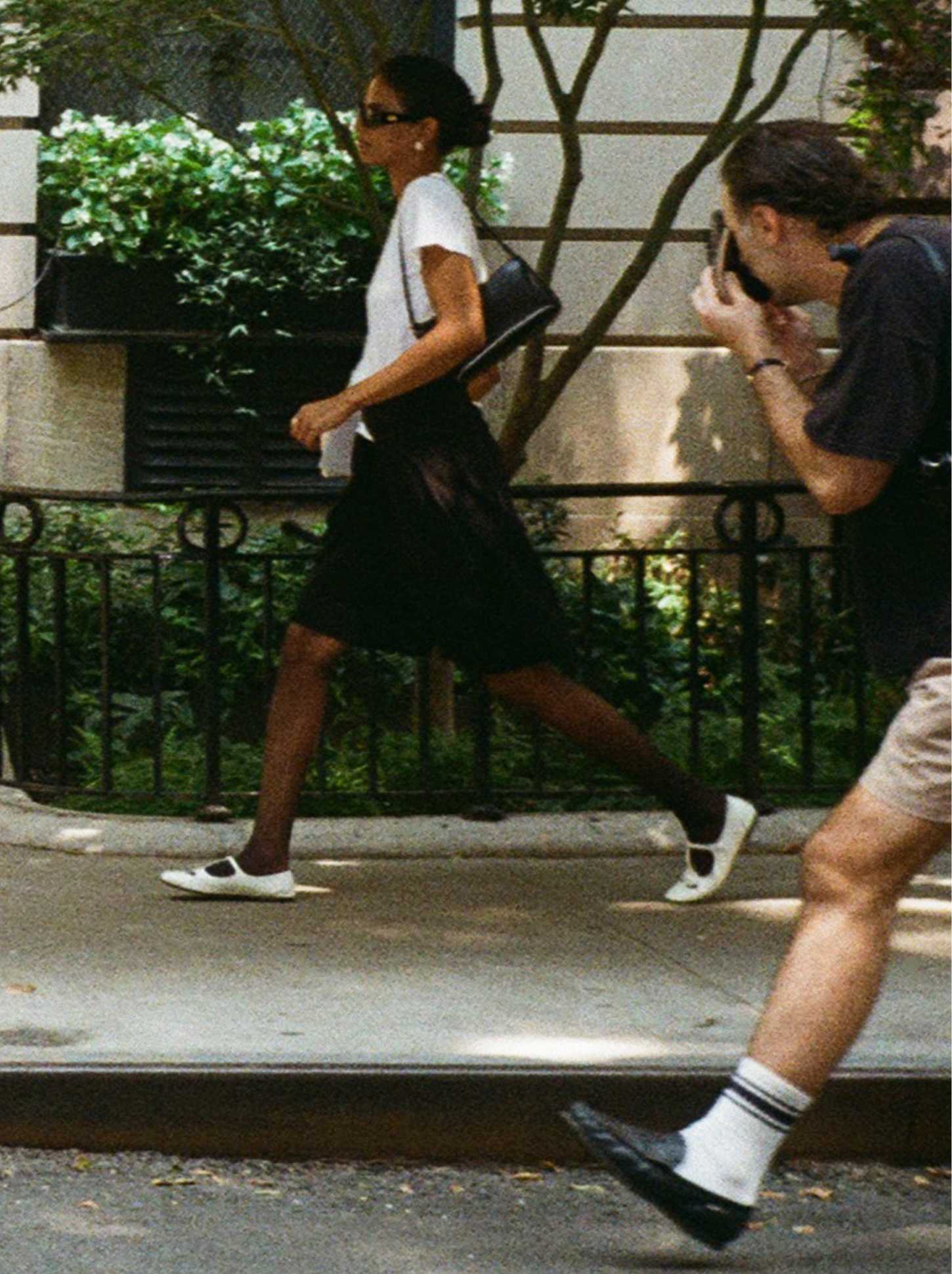 Woman on sidewalk with man taking her photo