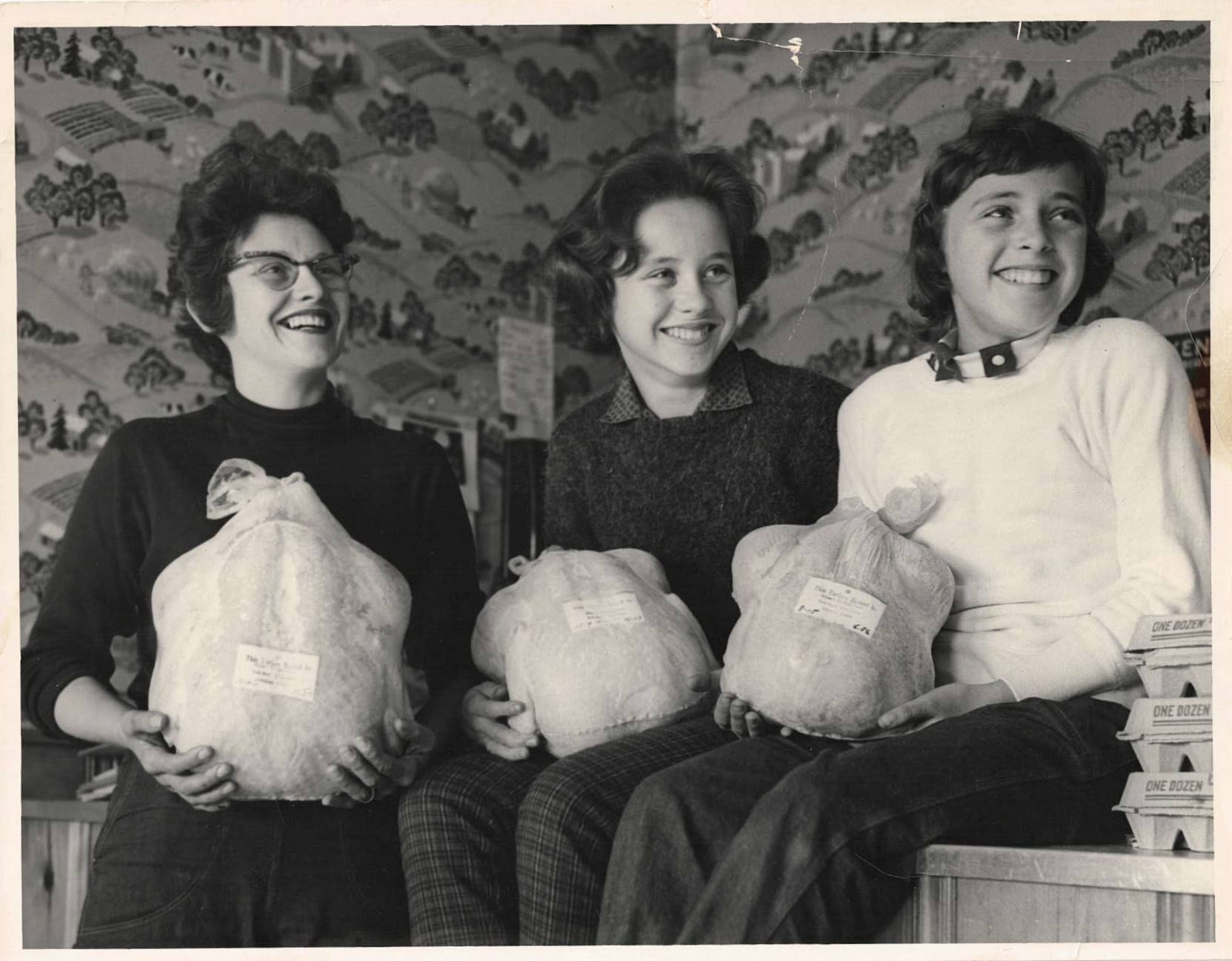 Black and white photo of three women holding turkeys.