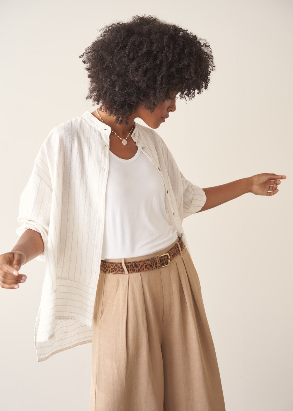 Woman wearing a white striped shirt and beige wide leg trousers against a plain background.