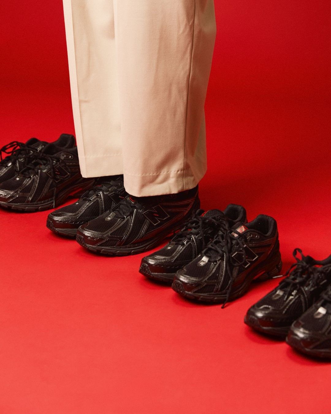 Person standing in black shoes with additional pairs on a red background.